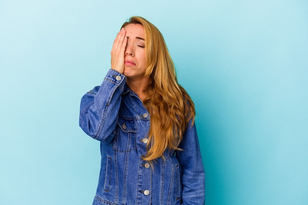 Mulher caucasiana, isolada em um fundo azul, cansada e com muito sono, mantendo a mão na cabeça.