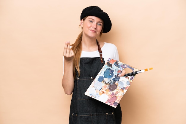 Mulher caucasiana jovem artista segurando uma paleta isolada em fundo bege fazendo gesto de dinheiro