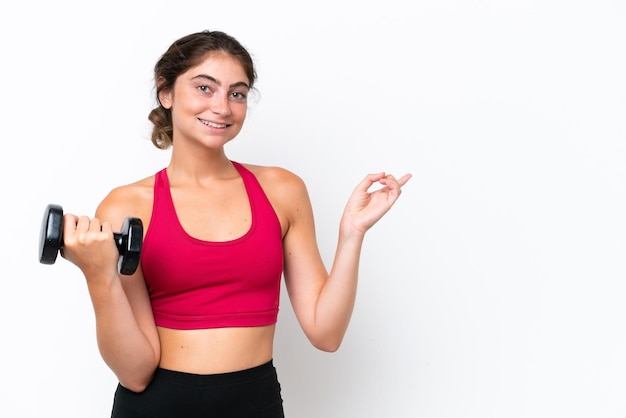 Mulher caucasiana jovem esporte fazendo levantamento de peso isolado no fundo branco, apontando o dedo para o lado