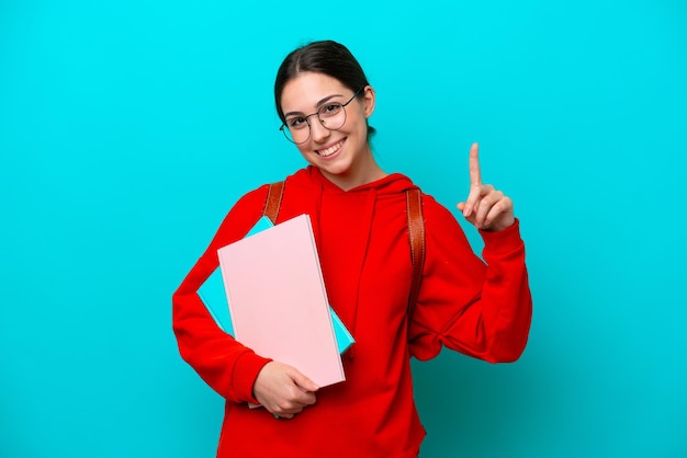 Mulher caucasiana jovem estudante isolada em fundo azul mostrando e levantando um dedo em sinal do melhor