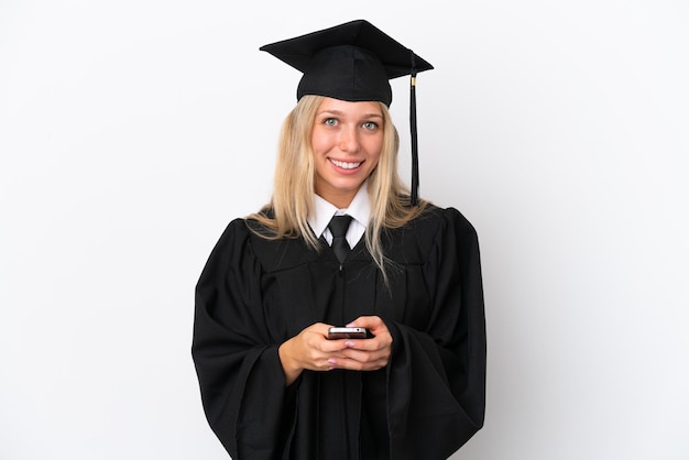 Foto mulher caucasiana, jovem, graduada em universidade, isolada no fundo branco, enviando uma mensagem com o celular