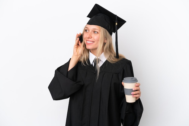 Mulher caucasiana jovem graduada na universidade isolada em fundo branco segurando café para levar e um celular