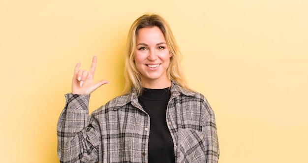 Mulher caucasiana loira se sentindo feliz divertida confiante positiva e rebelde fazendo sinal de rock ou heavy metal com a mão