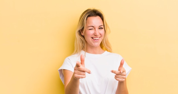 Mulher caucasiana loira se sentindo feliz, satisfeita, relaxada e bem-sucedida, apontando para a câmera escolhendo você