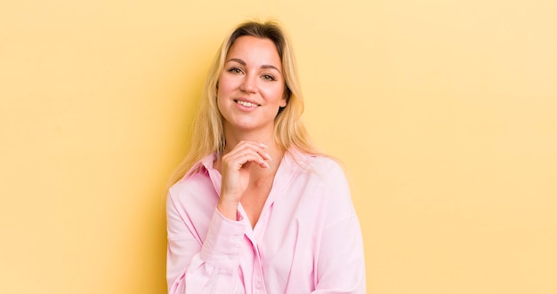 Mulher caucasiana loira sorrindo curtindo a vida se sentindo feliz amigável satisfeita e despreocupada com a mão no queixo