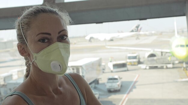 Mulher caucasiana no aeroporto com máscara médica protetora na cabeça contra o fundo do avião Conceito segurança em saúde proteção contra vírus epidemia de coronavírus sarscov2 covid19 2019ncov