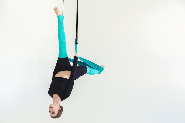 Mulher caucasiana, praticando fly yoga asana sobre fundo branco no estúdio de fitness, copie o espaço. Saúde, esporte, conceito de ioga