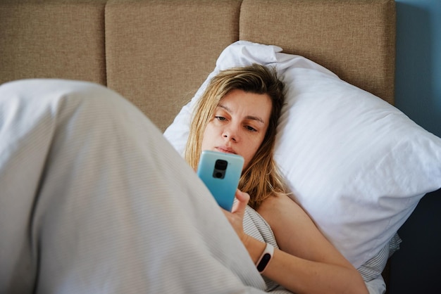 Mulher caucasiana relaxante na cama e usar smartphone