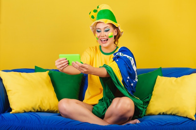 Mulher caucasiana ruiva brasileira fã de futebol brasileira no sofá assistindo jogo pelo smartphone