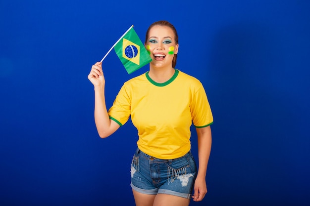 Foto mulher caucasiana ruiva fã de futebol brasileira fundo azul brasileiro acenando bandeira do brasil