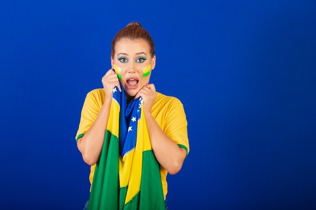 Mulher caucasiana ruiva fã de futebol do brasil fundo azul brasileiro ansioso e angustiado com a bandeira nas mãos