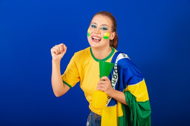 Mulher caucasiana ruiva fã de futebol do Brasil Fundo azul brasileiro dançando com bandeira e buzina
