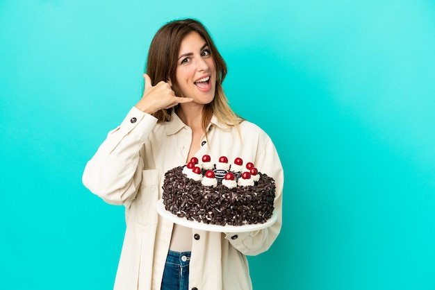 Mulher caucasiana, segurando o bolo de aniversário isolado no fundo azul, fazendo gesto de telefone. Ligue-me de volta sinal