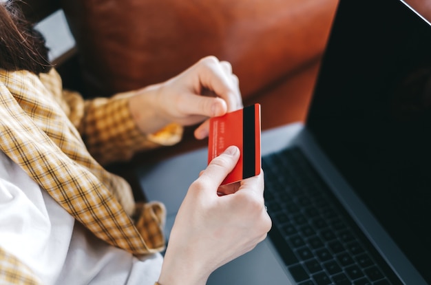 Mulher caucasiana, segurando o cartão de crédito, usando o laptop e fazendo compras online.