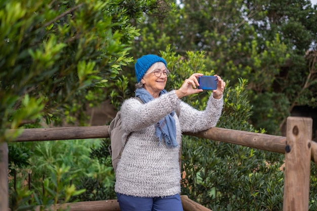 Mulher caucasiana sênior em caminhada tira uma fotografia com telefone desfrutando de liberdade e natureza Mulher idosa ativa em uma viagem de lazer admirando a paisagem