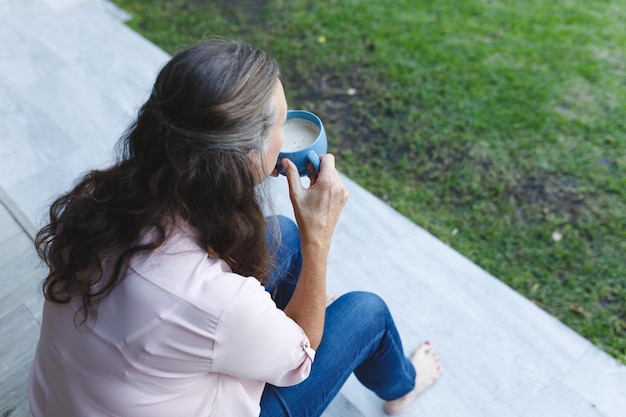 Mulher caucasiana sênior feliz sentada na escada, tomando café no jardim. estilo de vida de aposentadoria, passando um tempo sozinho em casa.