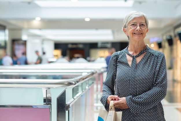 Mulher caucasiana sênior gostando de fazer compras em um shopping da cidade sorrindo para a câmera segurando a sacola de compras