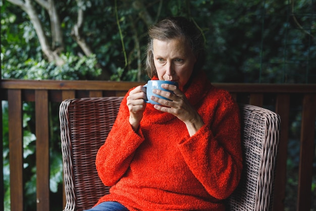 Mulher caucasiana sênior pensativa sentada na cadeira, tomando café no jardim. estilo de vida de aposentadoria, passando um tempo sozinho em casa.