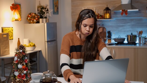 Mulher caucasiana sentada à mesa da cozinha com laptop