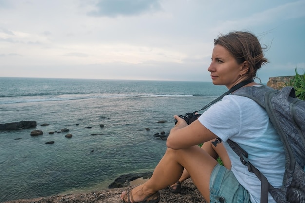 Mulher caucasiana sentada em uma pedra e olhando para o oceano