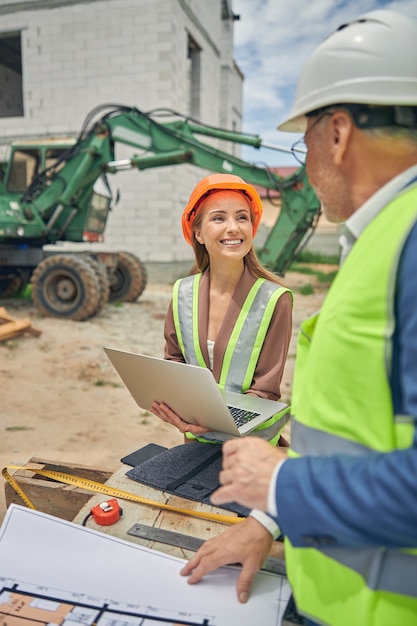 Mulher caucasiana sorridente com um laptop nas mãos e olhando para um engenheiro civil