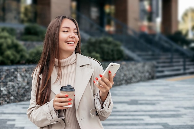 mulher caucasiana sorrindo usa um telefone celular e senta-se contra o pano de fundo de um prédio de escritórios