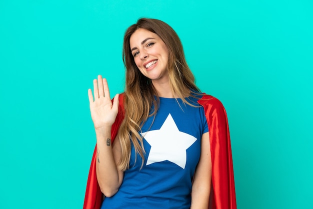 Mulher caucasiana super-heroína isolada em fundo azul, saudando com a mão e expressão feliz