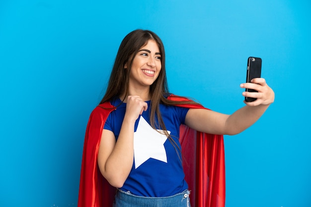 Mulher caucasiana super-heroína isolada em um fundo azul fazendo uma selfie