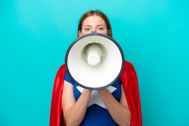 Mulher caucasiana super-heroína isolada em um fundo azul gritando em um megafone