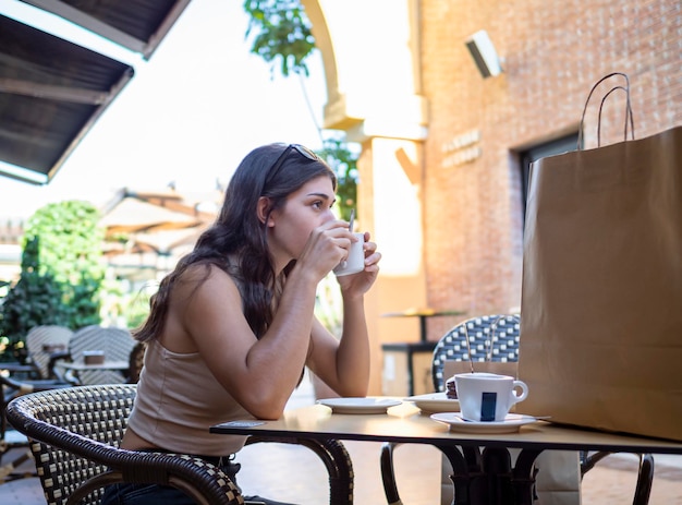 Mulher caucasiana tomando um café na rua sentado em um café depois de fazer compras relaxando e descansando