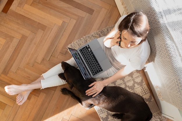 mulher caucasiana trabalhando em casa em um laptop sentada no chão do escritório em casa cachorro dormindo ao lado de uma mulher