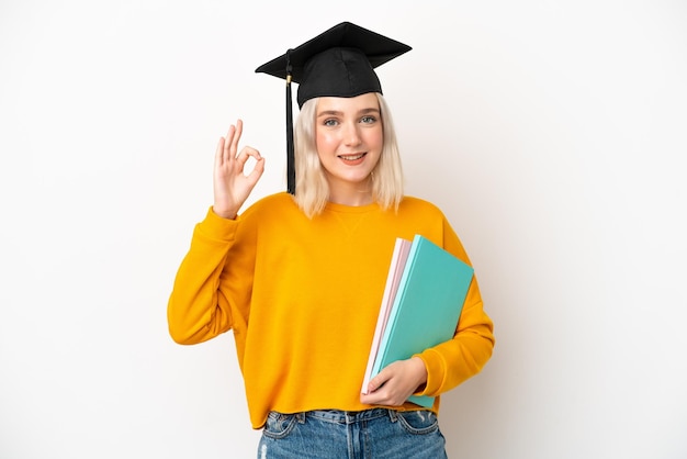 Mulher caucasiana universitária jovem graduada isolada em fundo branco mostrando sinal de ok com os dedos