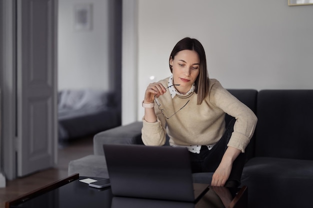 Mulher caucasiana usando laptop enquanto está sentado no sofá em casa na sala de estar à noite