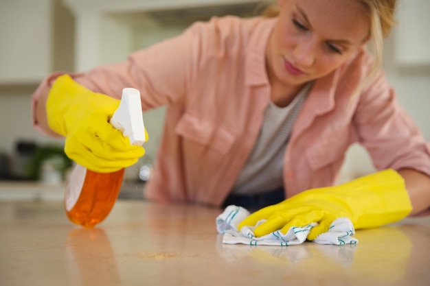 Mulher caucasiana usando luvas de borracha limpando bancada de cozinha com pano e spray. saúde e higiene em casa.