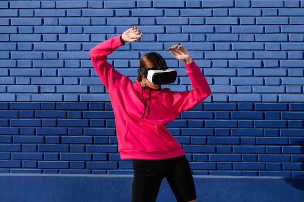 Mulher caucasiana usando óculos de realidade virtual na rua em um fundo de tijolos azuis