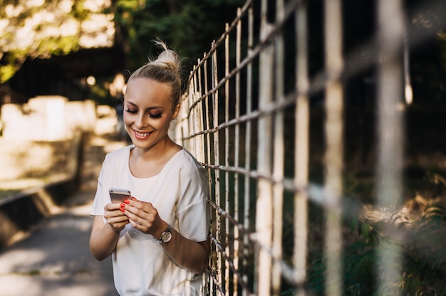 Mulher caucasiano loura bonita nova que guarda um telefone esperto e texting.