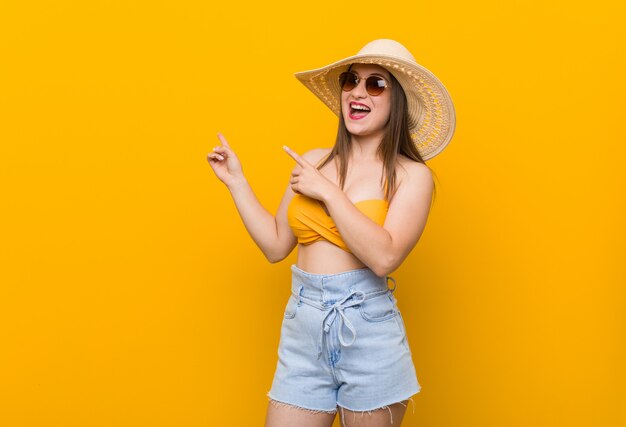 Mulher caucasiano nova que veste um chapéu de palha, olhar do verão entusiasmado guardando um espaço da cópia na palma.