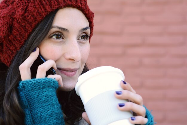 Mulher chamando no telefone celular e segurando uma xícara de café.