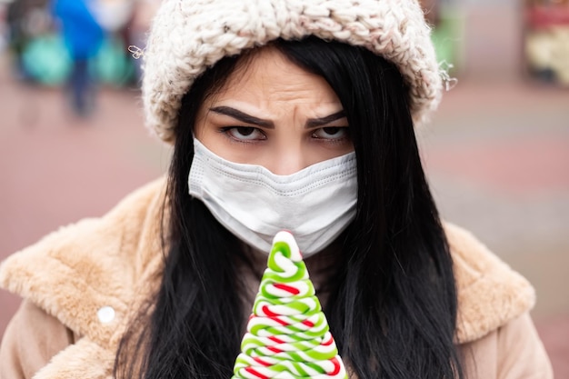 Mulher chateada com máscara facial segurando bala enquanto está na feira de férias de inverno