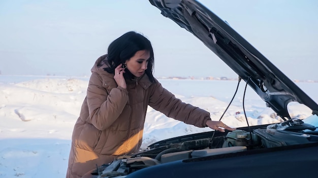 Mulher chateada olhando para motor quebrado em estrada com neve