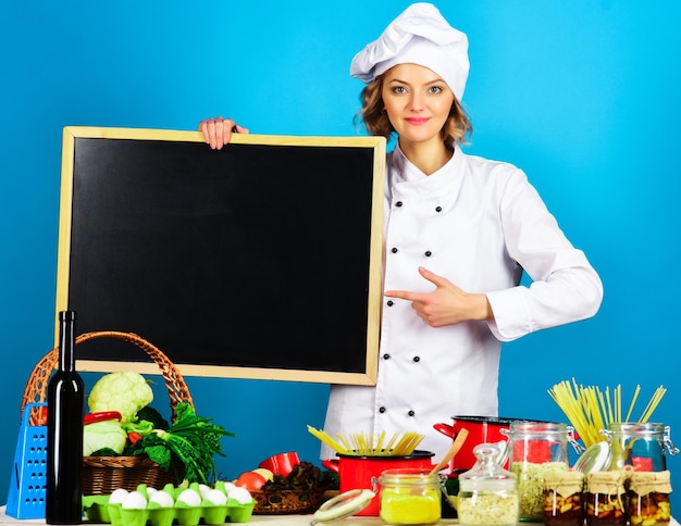 Mulher chef apontando o dedo para o quadro em branco preparação de alimentos cozinheira em uniforme de chef com