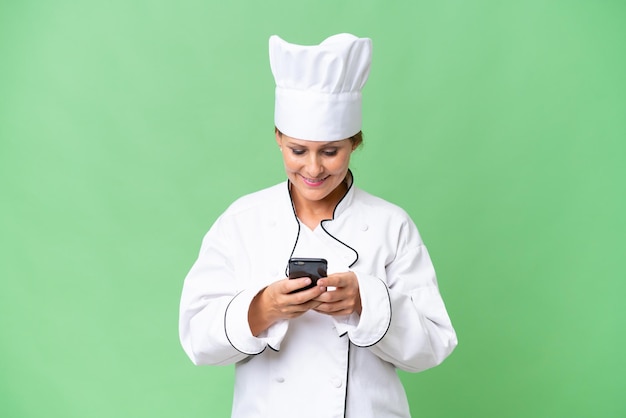 Mulher chef de meia idade sobre fundo isolado, enviando uma mensagem com o celular