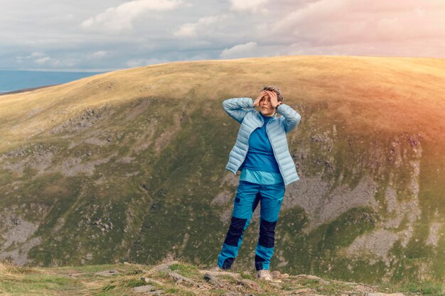 Mulher chegando ao destino e no topo da montanha contra um céu azul nublado no outono