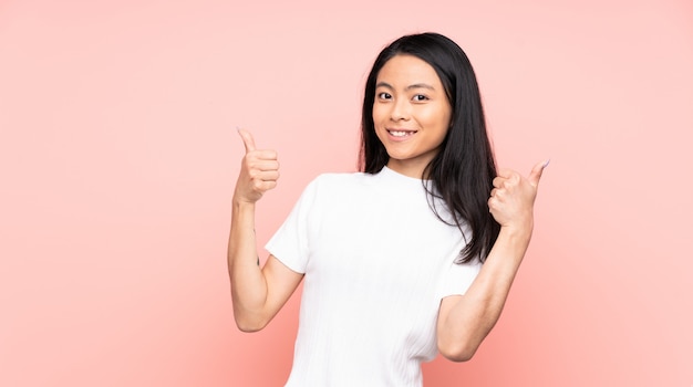 Mulher chinesa adolescente na parede rosa, dando um polegar para cima gesto