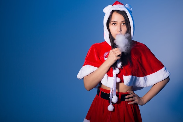 Mulher chinesa com fantasia de papai noel fumando cigarro eletrônico sobre fundo azul