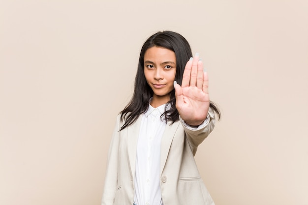 Mulher chinesa de negócios jovem em pé com a mão estendida, mostrando o sinal de stop, impedindo-o.