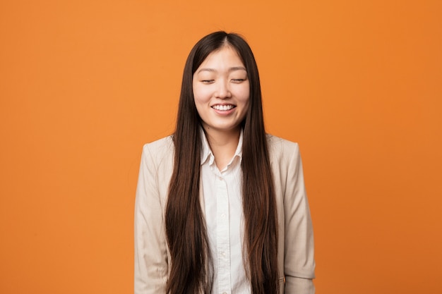 Mulher chinesa de negócios jovem ri e fecha os olhos, sente-se relaxado e feliz.