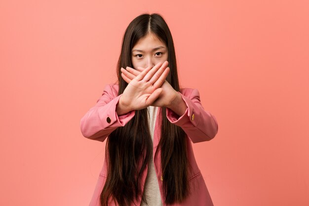 Mulher chinesa de negócios jovem vestindo terno rosa, fazendo um gesto de negação
