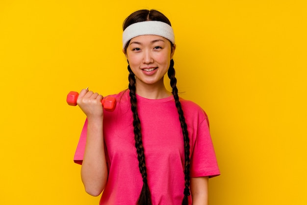 Mulher chinesa do esporte jovem isolada na parede amarela feliz, sorridente e alegre.