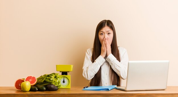 Mulher chinesa jovem nutricionista trabalhando com seu laptop assustado e com medo.